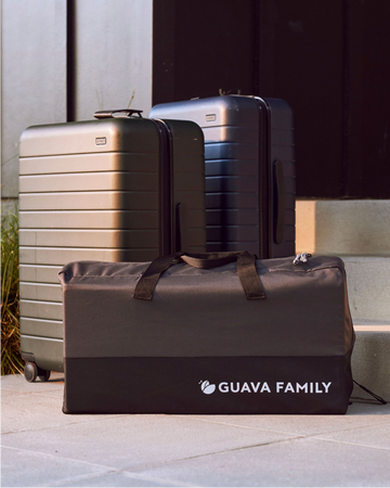 The Lotus Travel Crib packed away in it's carrying case placed next to some suitcases